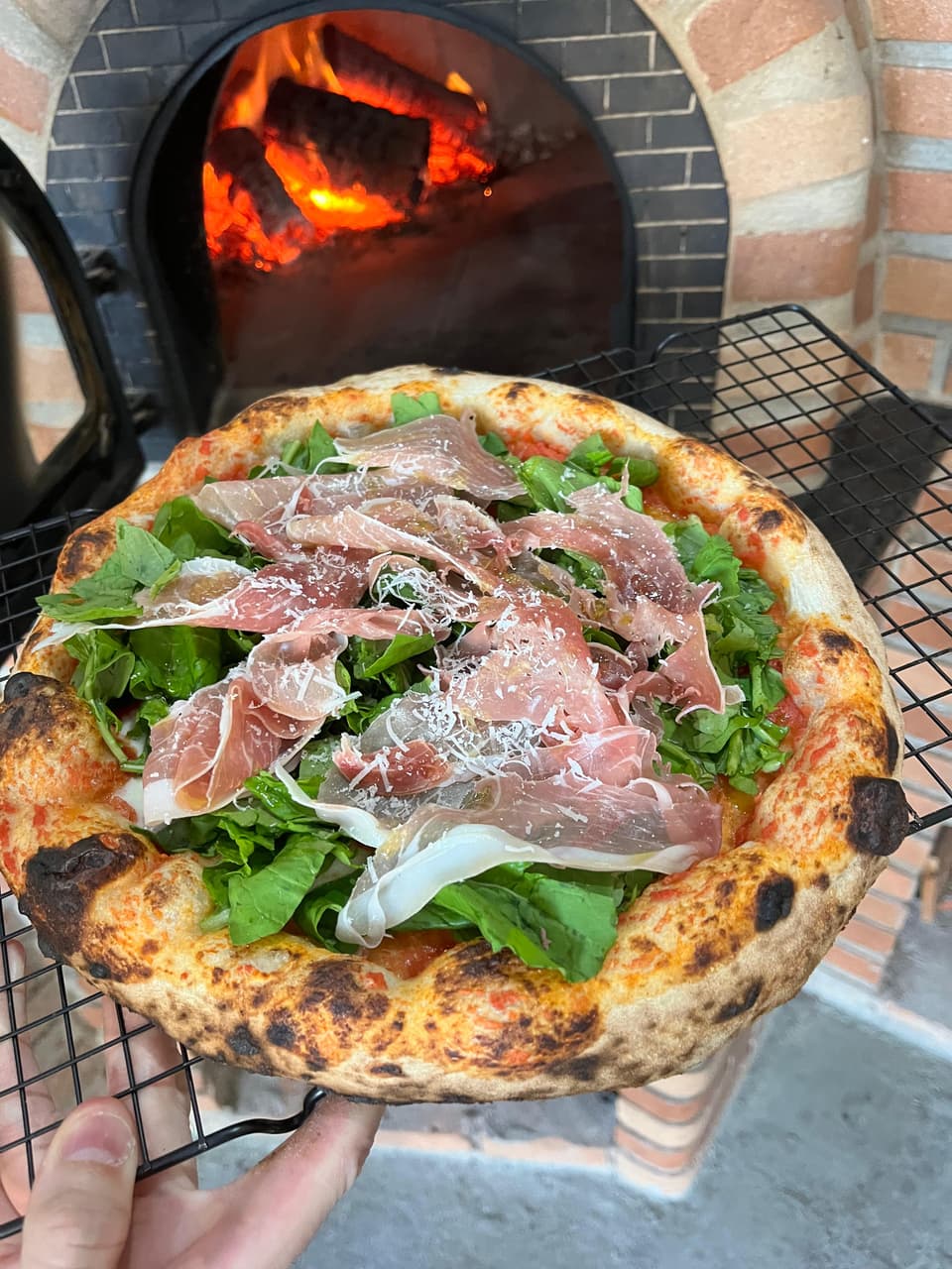 Pizza napolitana com presunto parma, rúcula e parmesão em frente ao forno a lenha